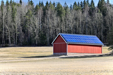 Rural landscape with a red farm building with solar roof. Production of sustainable energy in the countryside. Copy space.