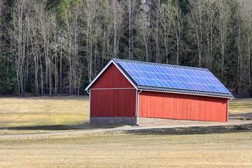 Rural landscape with a red farm building with solar roof. Production of sustainable energy in the countryside. 