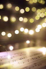 Old sheet with Christmas music notes as background against blurred lights. Christmas music concept