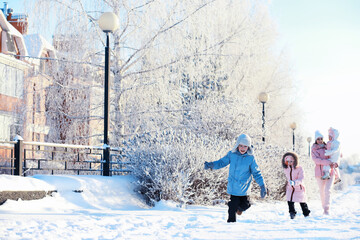 Family with children play snowy winter games in the park. Winter holidays and family vacation. Winter walk on the street on a sunny frosty day.