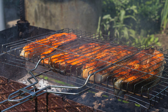 Grilling seasoned salmon fillets over open flames at a sunny outdoor barbecue