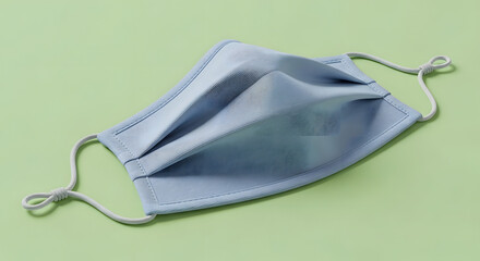 A light blue reusable cloth face mask with adjustable ear loops for personal protection against viruses and pollution, isolated on a solid green background
