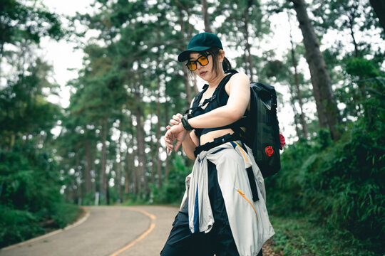 Adventurous Young Woman in Sportswear Checking Smartwatch While Hiking on a Scenic Trail Surrounded by Lush Green Trees and Nature