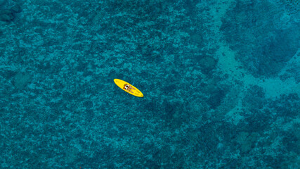 Aerial view woman bright yellow kayak with in the vast expanse of crystal clear turquoise water. The seabeds rocky texture is visible beneath the surface, concept marine environment	
