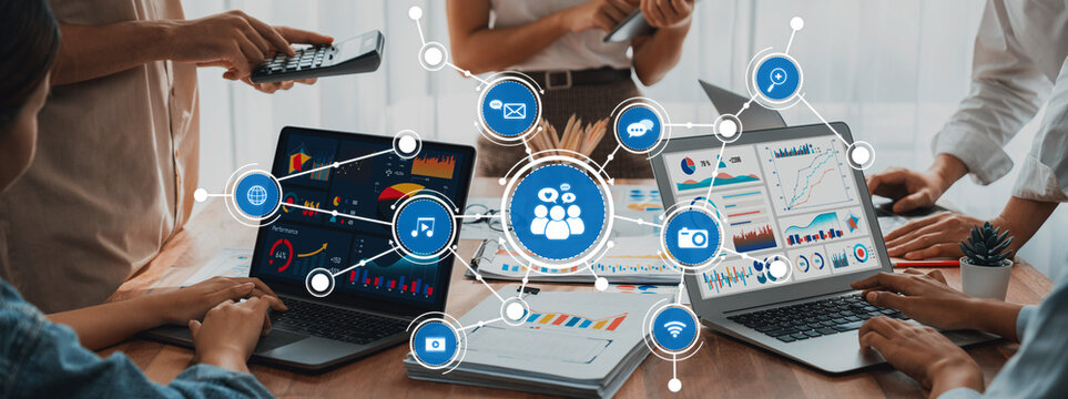 A dynamic workplace scene featuring diverse professionals collaborating with laptops and digital media, highlighting teamwork and communication in project management efforts. Amity - Powered by Adobe