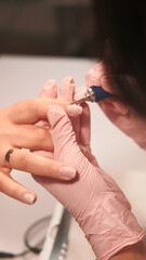 Gel nails. Professional manicure procedure. Female skilled manicurist hand removing client cuticle with milling machine woman treatment.