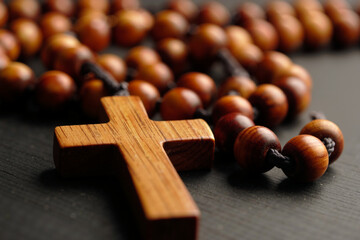 A wooden rosary with a prominent cross lays on a dark wooden surface, creating a serene ambiance. The texture and color of the beads reflect tranquility. Generative AI.
