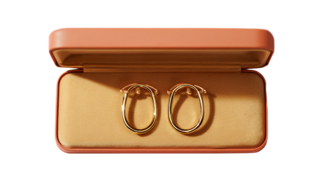 Elegant gold oval hoop earrings displayed inside an open peach jewelry box isolated on transparent background