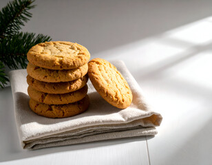 Stack of delicious peanut butter cookies artfully arranged on a light-colored cloth, with a hint of green pine in the background