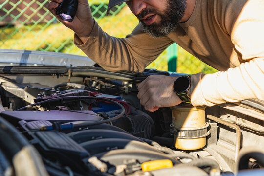 Man working on car engine with flashlight in bright outdoor setting - Powered by Adobe