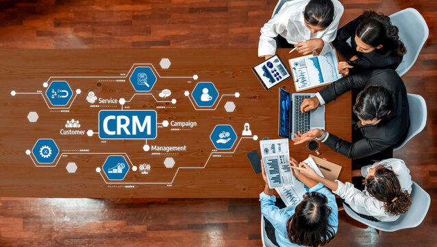 A diverse team of professionals collaborates on a CRM strategy, utilizing charts and digital tools to enhance business growth and customer service in a modern office. Amity - Powered by Adobe