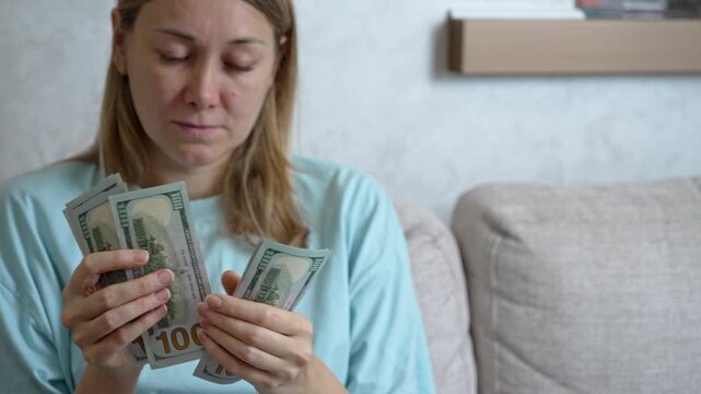 A woman sits on a soft couch in her living room, visibly worried as she counts her cash. High utility bills weigh heavily on her mind. Her concerned expression reflects the financial strain.