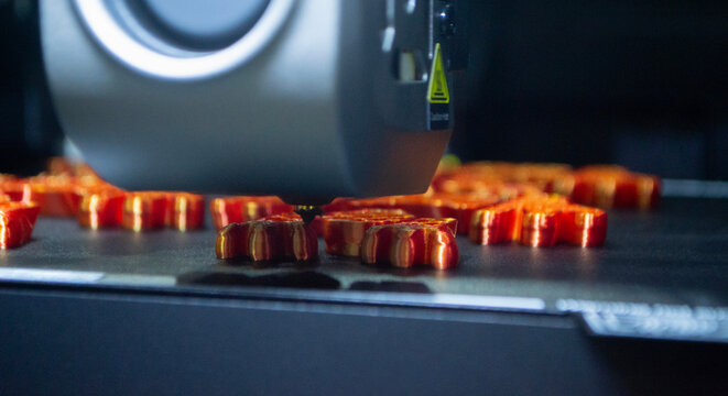 3D printer close up. Working 3D printer in process of printing object from molten orange plastic. 3D printer creating model by flowing liquid plastic from extruder of printer. 3D printing technology - Powered by Adobe