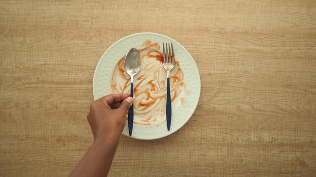 Empty plate with leftover sauce and a fork in hand