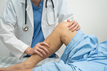 Doctor checking Asian elderly woman patient with scar knee replacement surgery in hospital.