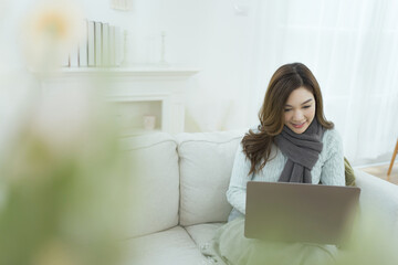 Naklejka premium Asian woman relaxing and using laptop computer on cozy sofa in living room.