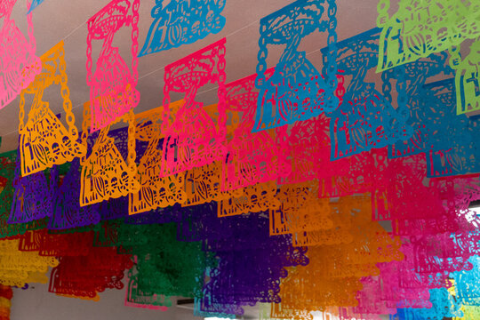 A colorful display of paper lanterns hangs from the ceiling. The lanterns are in various colors. Mexican Day of the Dead tradition, offerings, food, colors, decorations, and papel picado, La Catrina. - Powered by Adobe