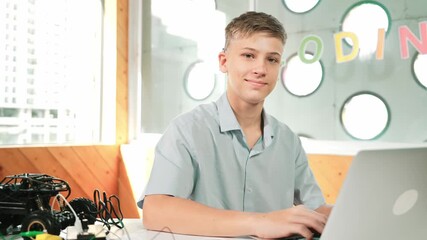 Smart teenager working on laptop and looking at camera at STEM technology class. Caucasian student using computer to analyze data while smiling with confident on table with car model. Edification - Powered by Adobe