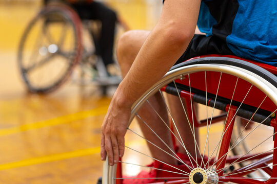 focus on one arm and wheelchair wheel with spokes and another blurry wheelchair in background