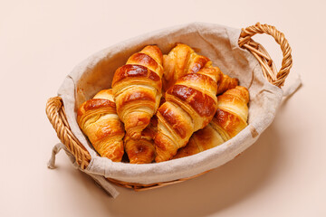 Freshly baked croissants in wicker basket on light background