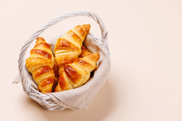 Freshly baked croissants in wicker basket on light background