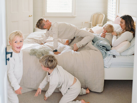 Young boys play and tumble around mum lying on the bed