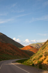 Vertical view of a curving road passing between mountainsides with vibrant orange and green slopes, with high snow-capped peaks visible in the far distance