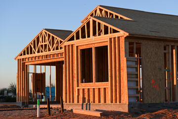 Obraz premium Wood framing structure of a single-family home under construction, showing early-phase residential building with exposed trusses, plumbing, and sheathing installation in progress