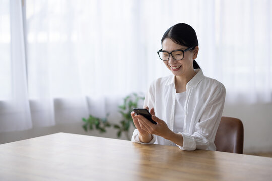 Smiling Woman with Glasses Using Smartphone at Table
