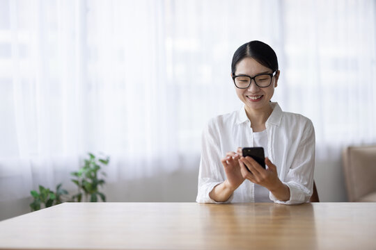 Smiling Woman with Glasses Using Smartphone at Table