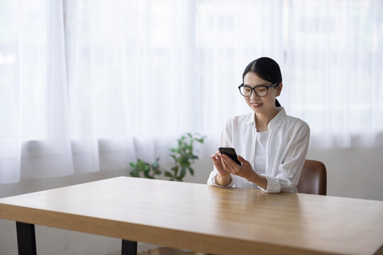 Smiling Woman with Glasses Using Smartphone at Table