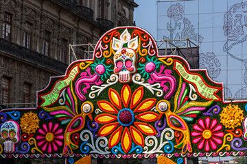 A colorful flower with a skull on top. The skull is surrounded by a bunch of flowers. Mexican Day of the Dead tradition, offerings, food, colors, decorations, and papel picado, La Catrina.