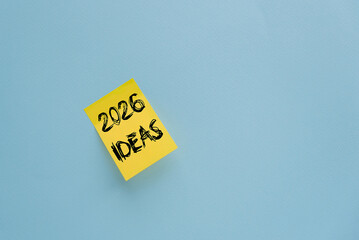 A yellow sticky note with the text '2026 IDEAS' written in black on a light blue background. The...