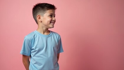 Little boy wears light blue athletic tee shirt. Smiles naturally, looks sideways with confident expression. Young male child poses happy, relaxed against pink background. Kid shows positive attitude