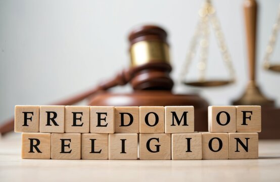 Wooden blocks display Freedom of Religion with gavel. It symbolizes legal and justice aspects. Scales behind convey balance under law for religious liberty and rights issues. Gavel means democracy.
