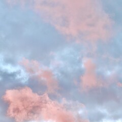 A dreamlike atmospheric scene where a dramatic mass of pink and peach clouds glows against a pale mauve and blue sky during sunset or sunrise, filling the frame with pastel colors.