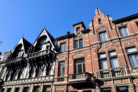Historic European townhouses: one half-timbered style, the other red brick Neo-Renaissance, featuring intricate gables against a clear blue sky in Antwerp, Belgium