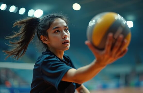 Young woman playing volleyball in indoor court. Female athlete focuses on yellow and black ball. Player in motion with blurred background. Active sportswoman in action with determination.