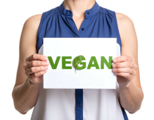 A person holds a white rectangular sign displaying "VEGAN" in green leafy letters, promoting plant-based eating