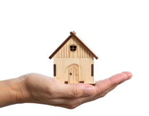 A person's hand, cupped and open, cradles a small wooden house against a stark black background