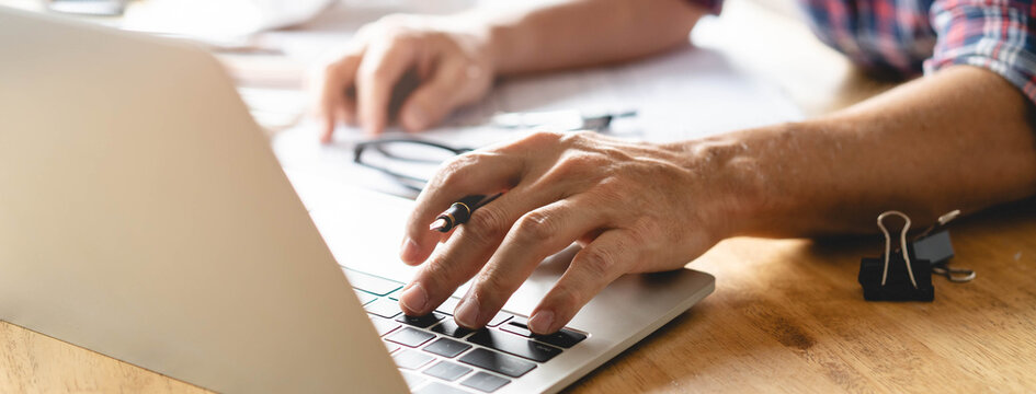 Close up view hands of architect working on the desk with laptop computer and checking material color of room to interior.