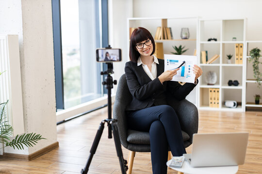 Caucasian woman, business professional, presenting growth graphs during vlog in modern office setup.