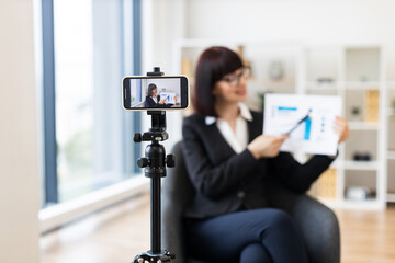 Caucasian woman in business suit recording video about revenue growth using graphs, modern office setup with natural light, professional presentation, concept communication and education.