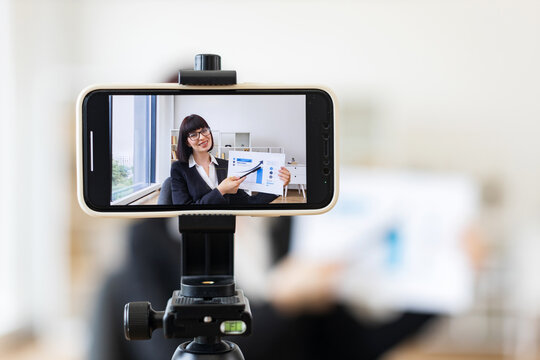 Caucasian woman presenting business charts and growth analysis while being recorded through smartphone setup