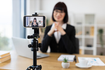Caucasian woman wearing suit recording video blog about business topics using mobile setup indoors