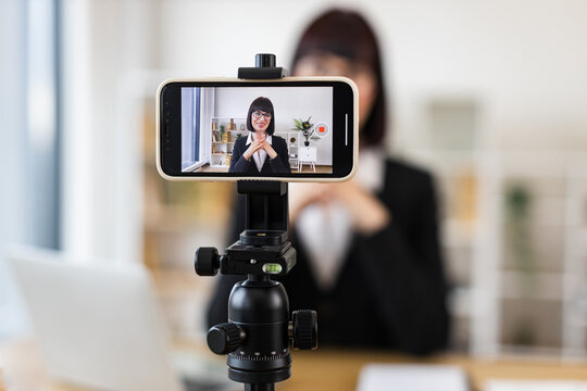 Caucasian woman wearing suit recording video blog about business topics using mobile setup indoors - Powered by Adobe