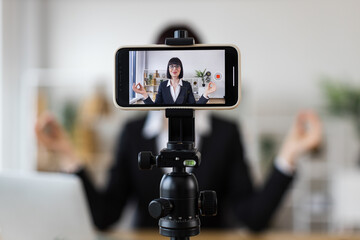 Caucasian adult woman practicing meditation at work, recording session using smartphone and tripod.