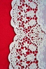 Close-up of white crochet lace with honeycomb and floral patterns on vibrant red fabric background, highlighting intricate handmade detail