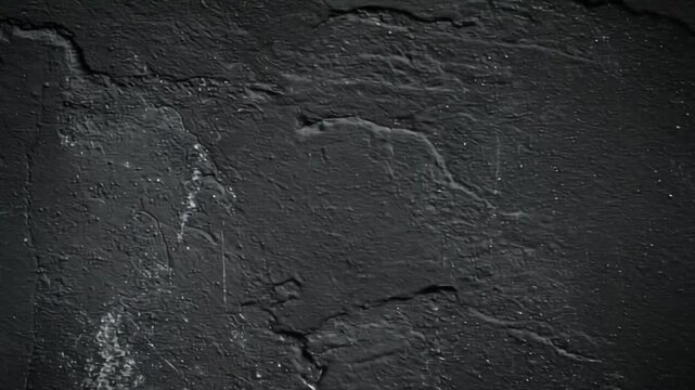 A textured, dark gray abstract background with rough and weathered appearance, showing cracks and spots