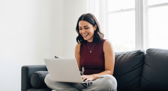 Woman sitting on couch, using laptop and smiling happily at home during daytime